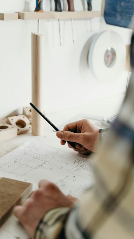 Focused hands of a carpenter sketching a design in a woodworking studio.